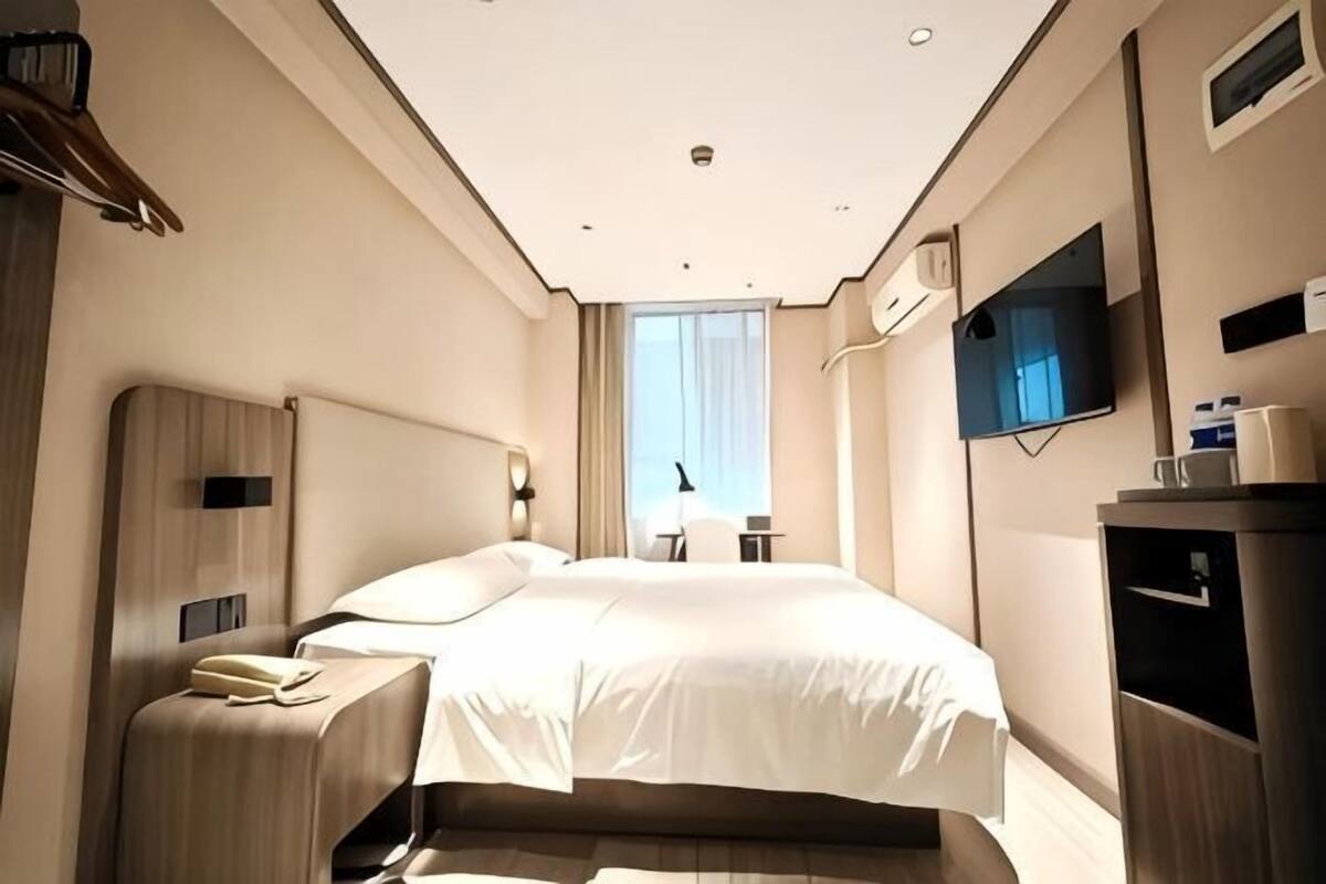 A hotel room with a large bed, bedside tables, a TV, a desk, and a window with curtains.