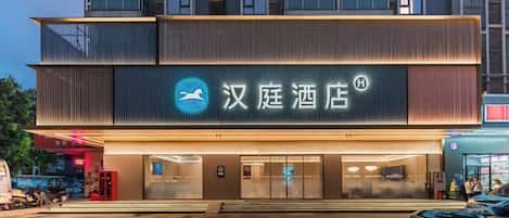A hotel with a modern facade, a prominent sign with Chinese characters, and a well-lit entrance.