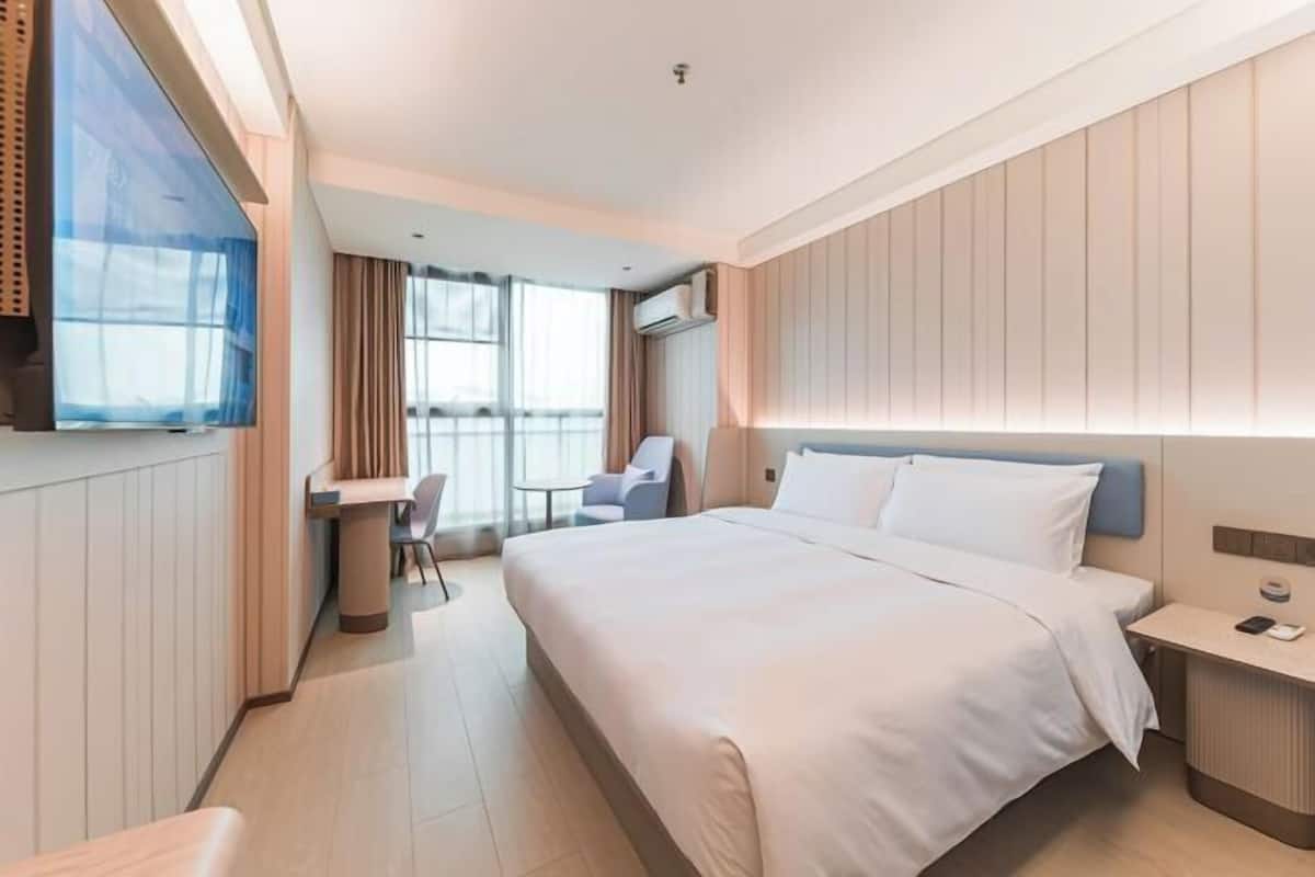 A modern hotel room with a large bed, a desk, a chair, and a TV.