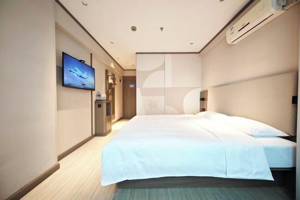 A hotel room with a large bed, a flat-screen TV mounted on the wall, and a modern air conditioning unit.