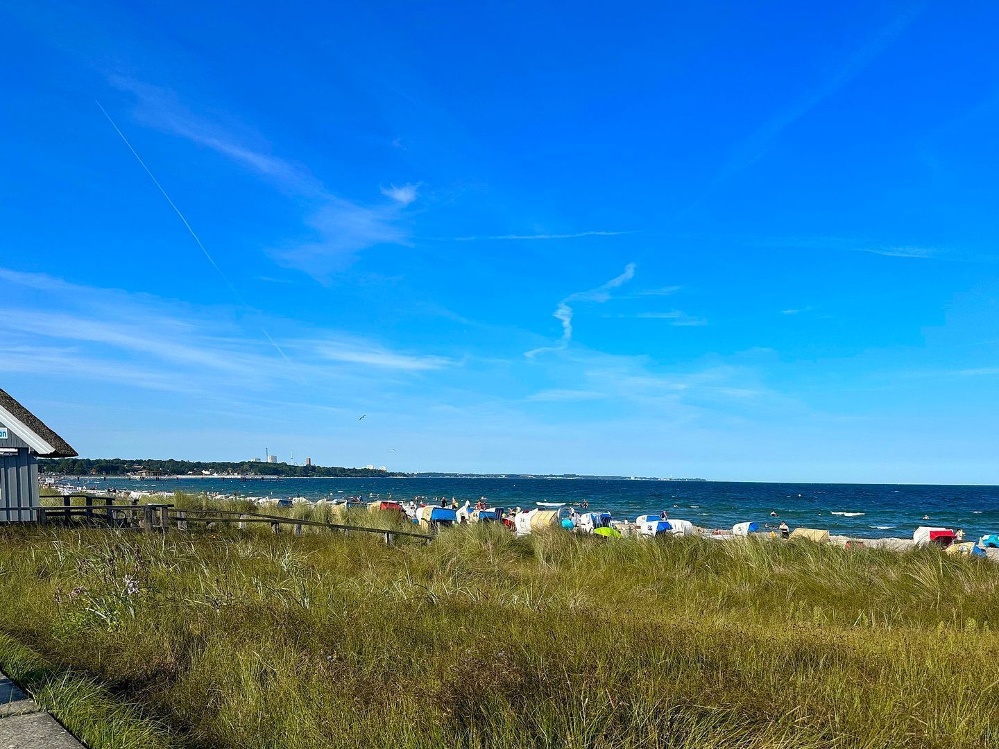A coastal view with a grassy foreground, a pier, and a beach with colorful umbrellas.