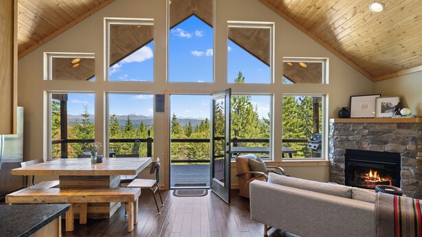 A spacious living area with a high ceiling, large windows, a stone fireplace, and a view of the outdoors.