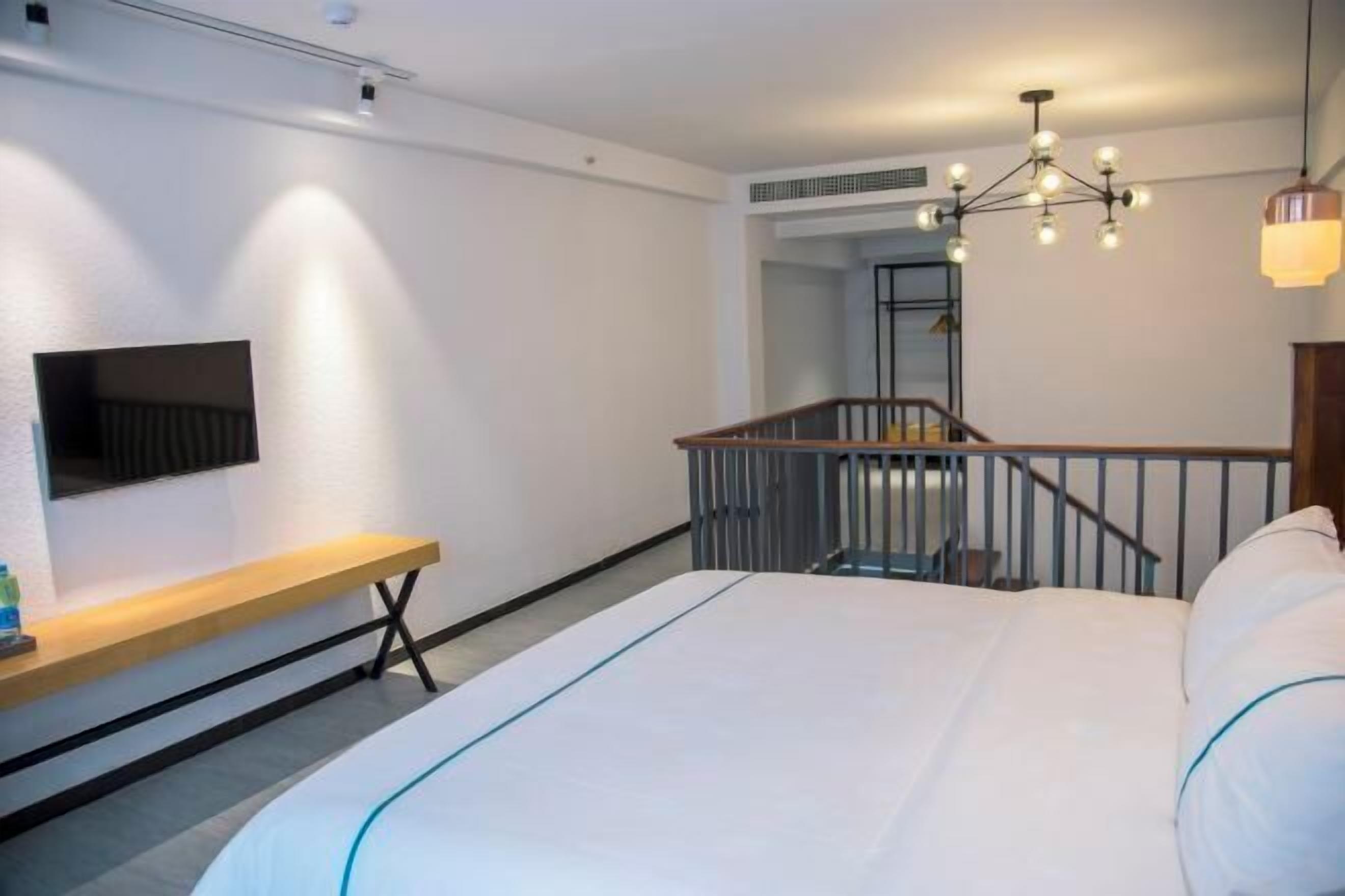 A modern hotel room with a large bed, a TV mounted on the wall, a bench, and a staircase.