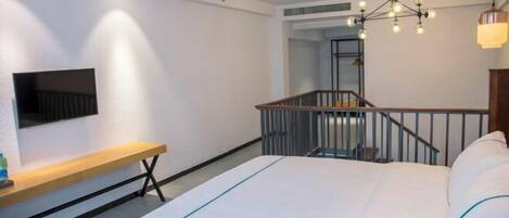 A modern hotel room with a large bed, a TV mounted on the wall, a bench, and a staircase.