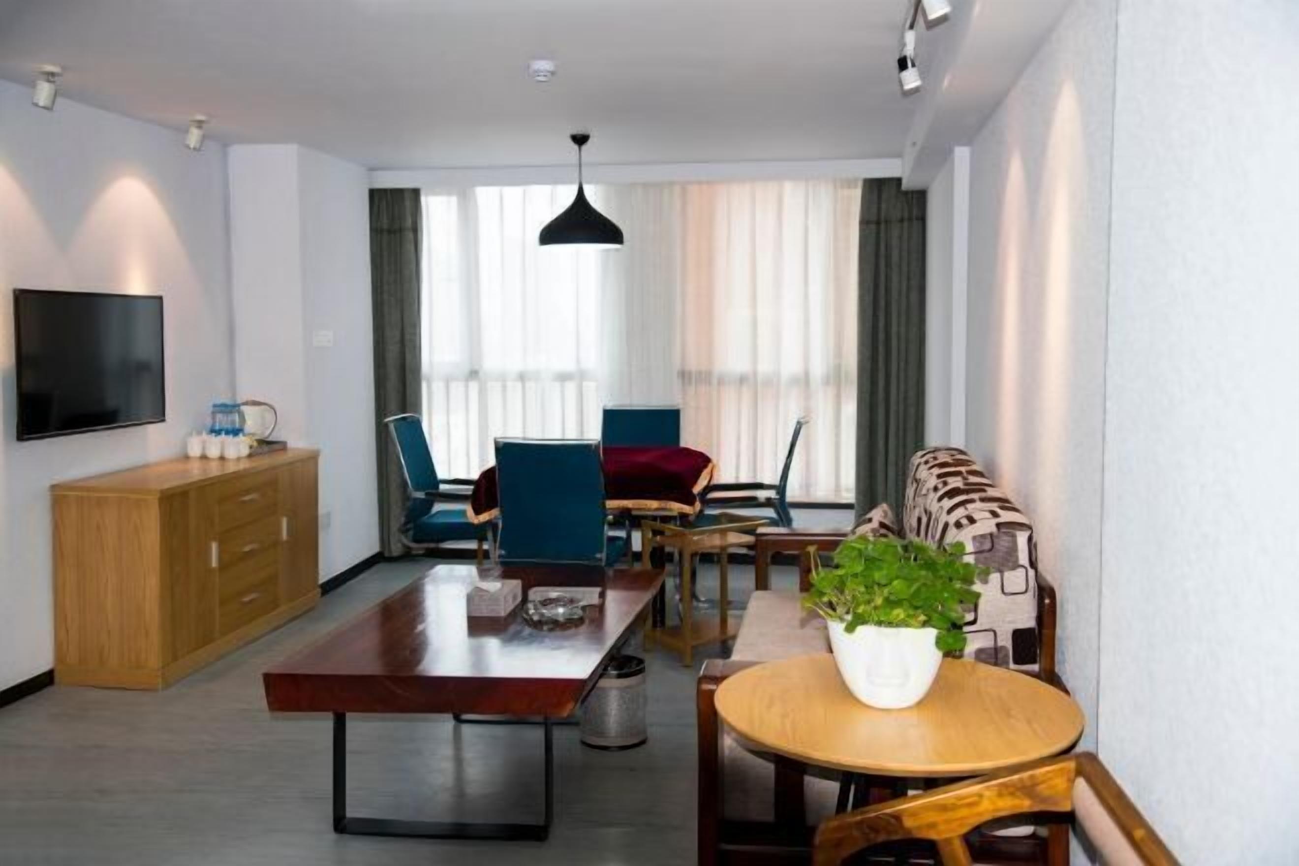 A modern living room with a flat-screen TV, wooden furniture, a dining table, and a potted plant.