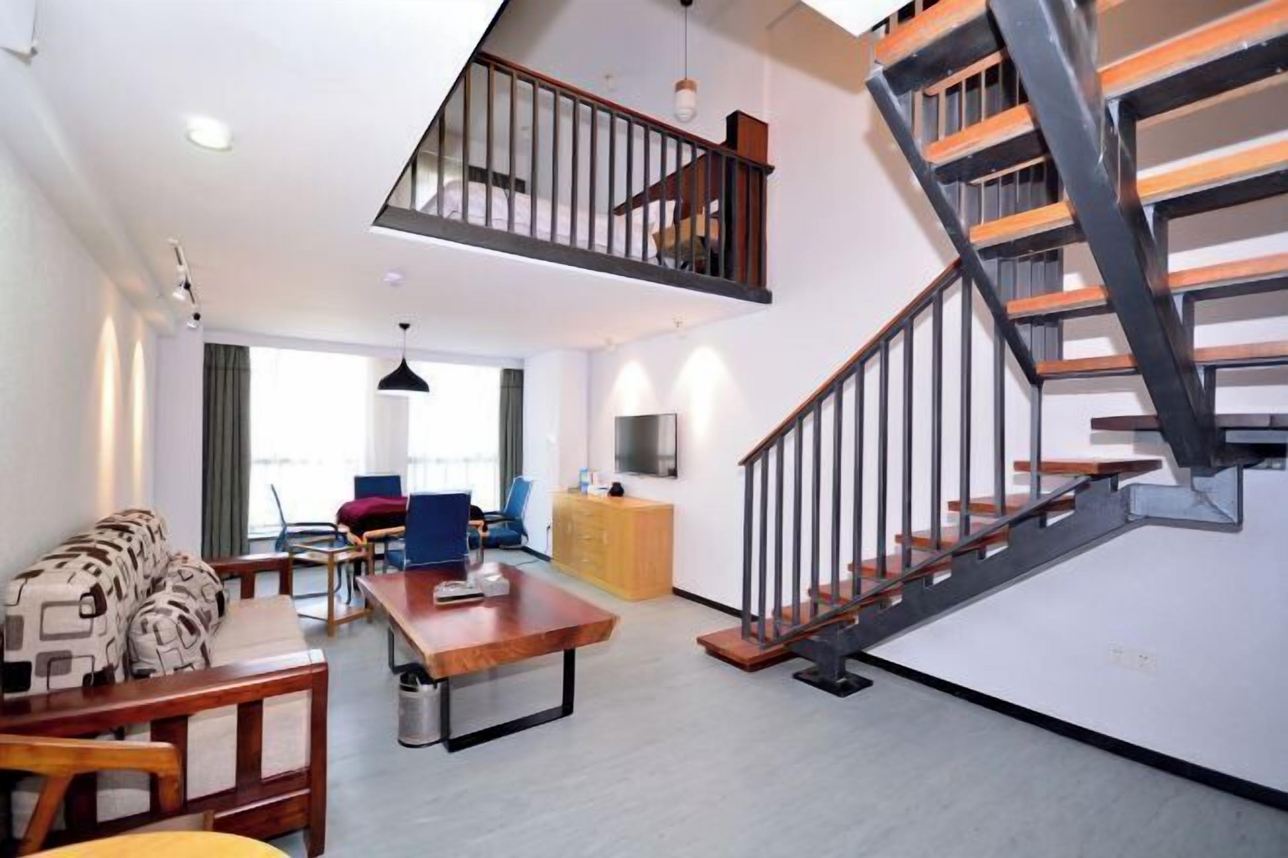 A modern living room with a wooden dining table, a sofa, and a staircase with a black railing.