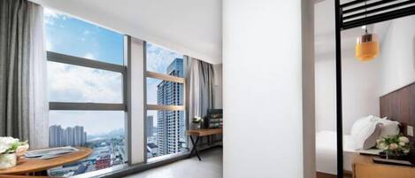 A modern hotel room with a large window, a dining area, and a small kitchenette.