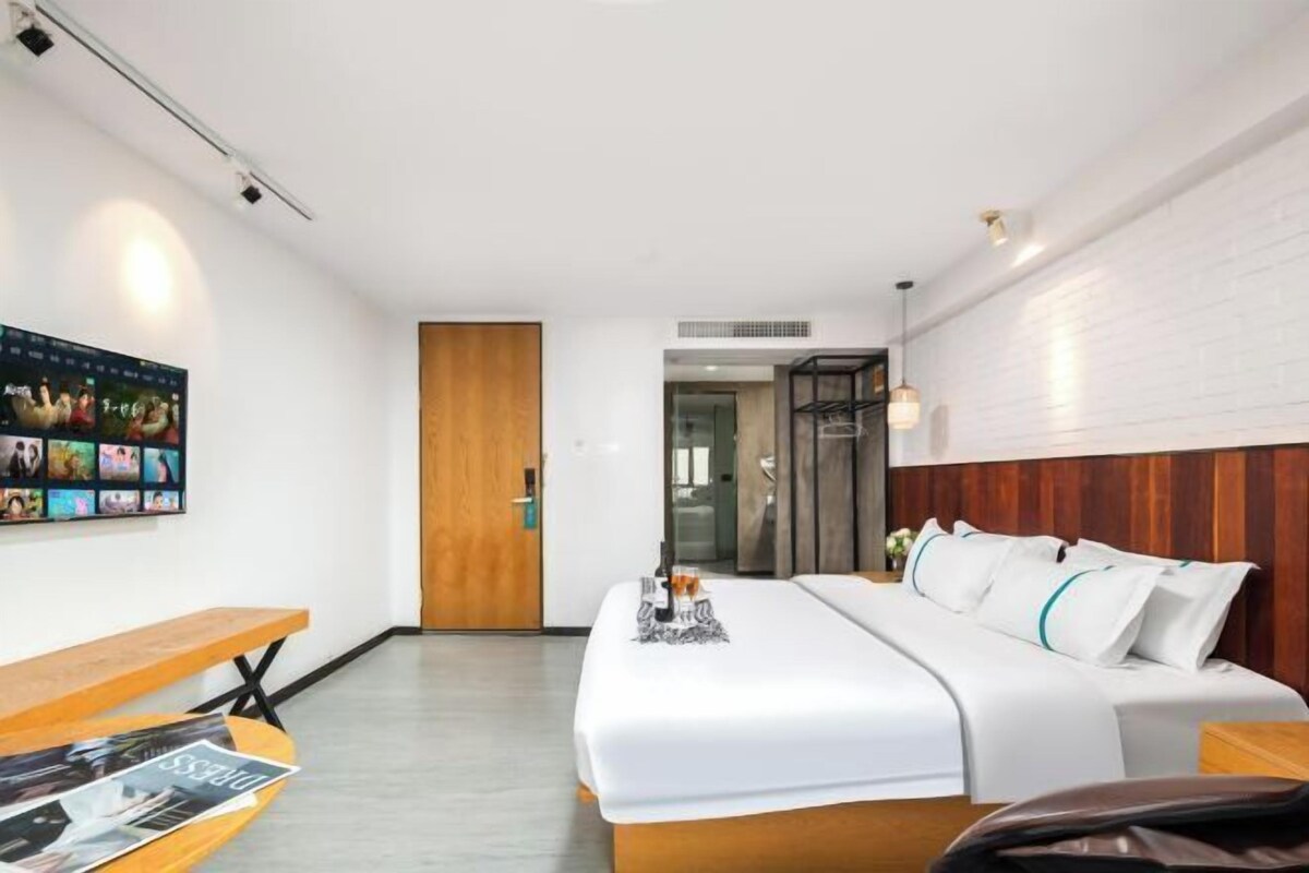 A modern hotel room with a large bed, a wooden bench, a wall-mounted TV, and a wooden door.
