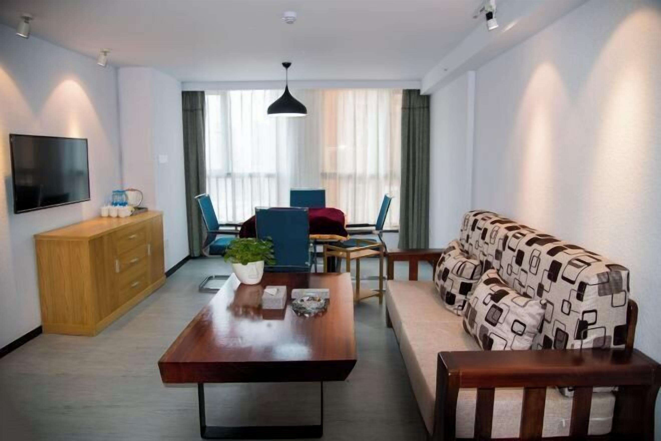 Ein modernes Wohnzimmer mit Couch und gemusterten Kissen, einem Holztisch, einem an der Wand montierten Fernseher sowie einem Essbereich mit Stühlen und Tisch.