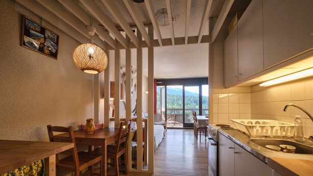 Una cocina moderna con una mesa de comedor de madera, sillas, una lámpara colgante y vistas a través de una puerta de vidrio.
