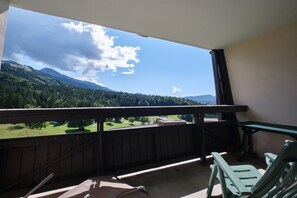 Uma varanda com vista para uma cadeia montanhosa arborizada e céu claro.