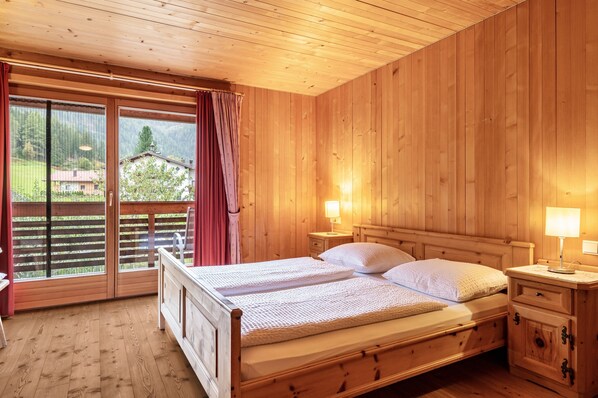 Ein Zimmer mit Holzwänden, einem Bett, zwei Nachttischen und einer Schiebetür zu einem Außenbereich.