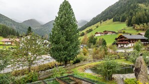 A mountainous landscape with traditional wooden houses, a large tree, and a small pond.