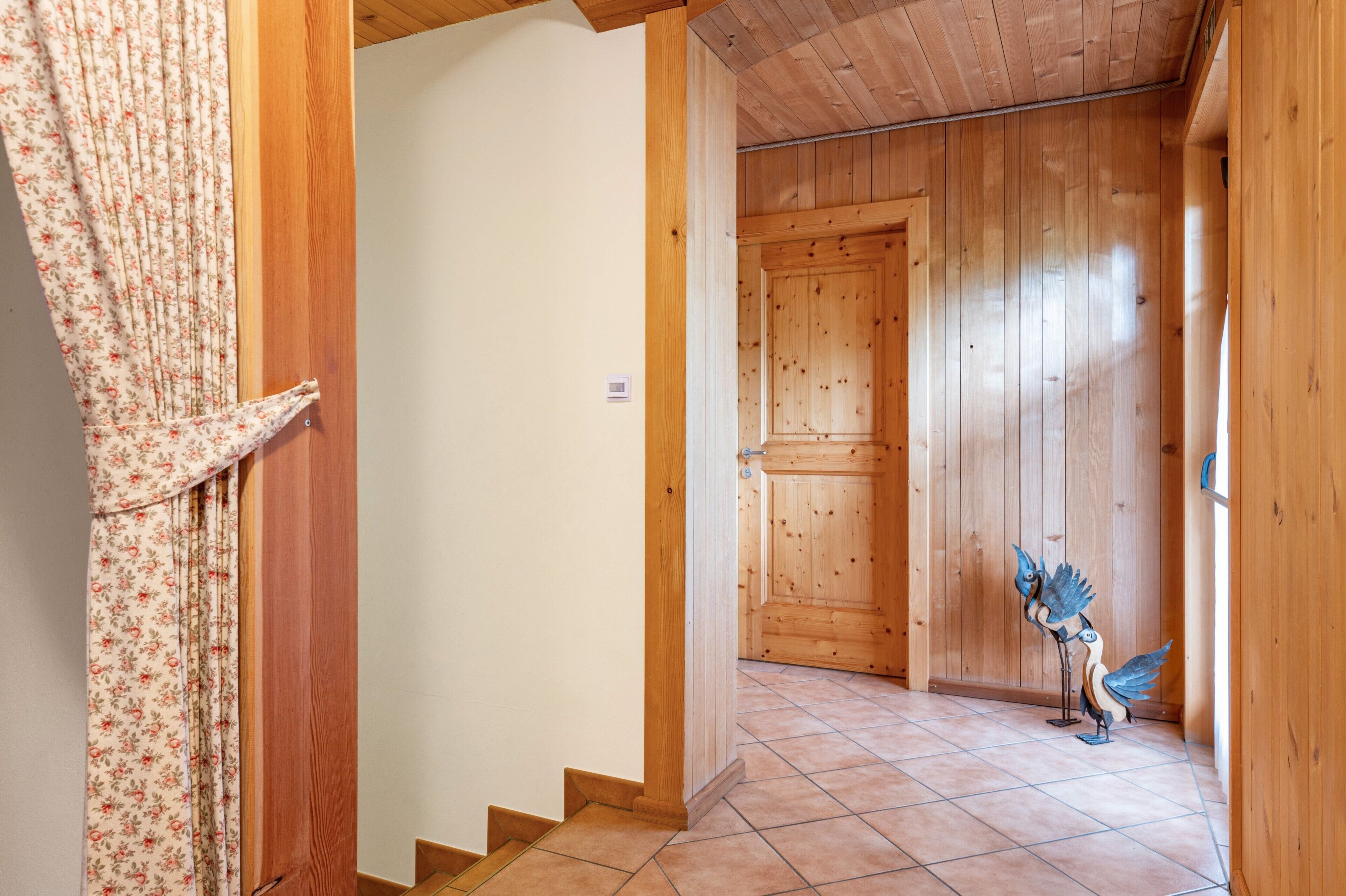 A wooden interior hallway with a door, a tiled floor, and a decorative bird sculpture.