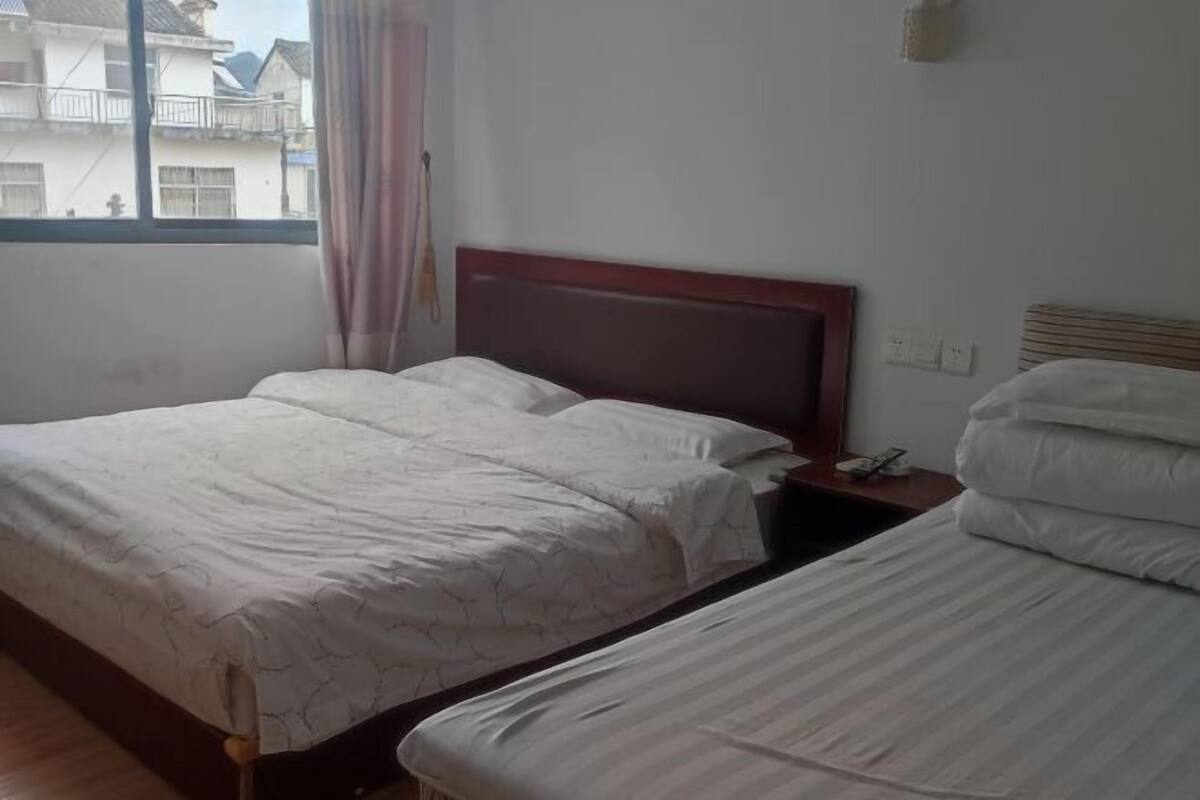 A hotel room with two beds, a wooden headboard, a bedside table with a phone, and a window with curtains.