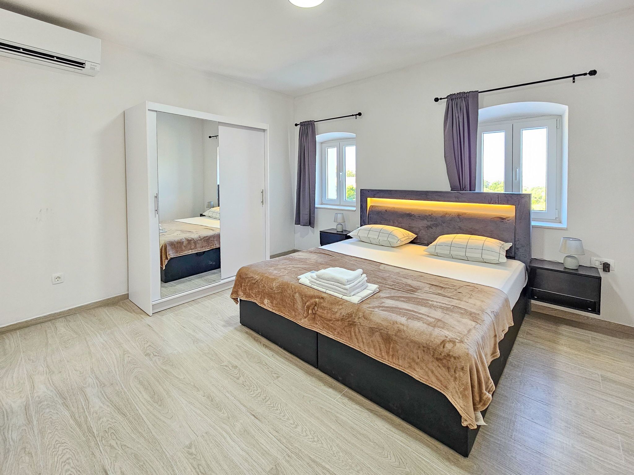 Ein Schlafzimmer mit Bett, Nachttischen, einem Kleiderschrank und einem Fenster mit Vorhängen.