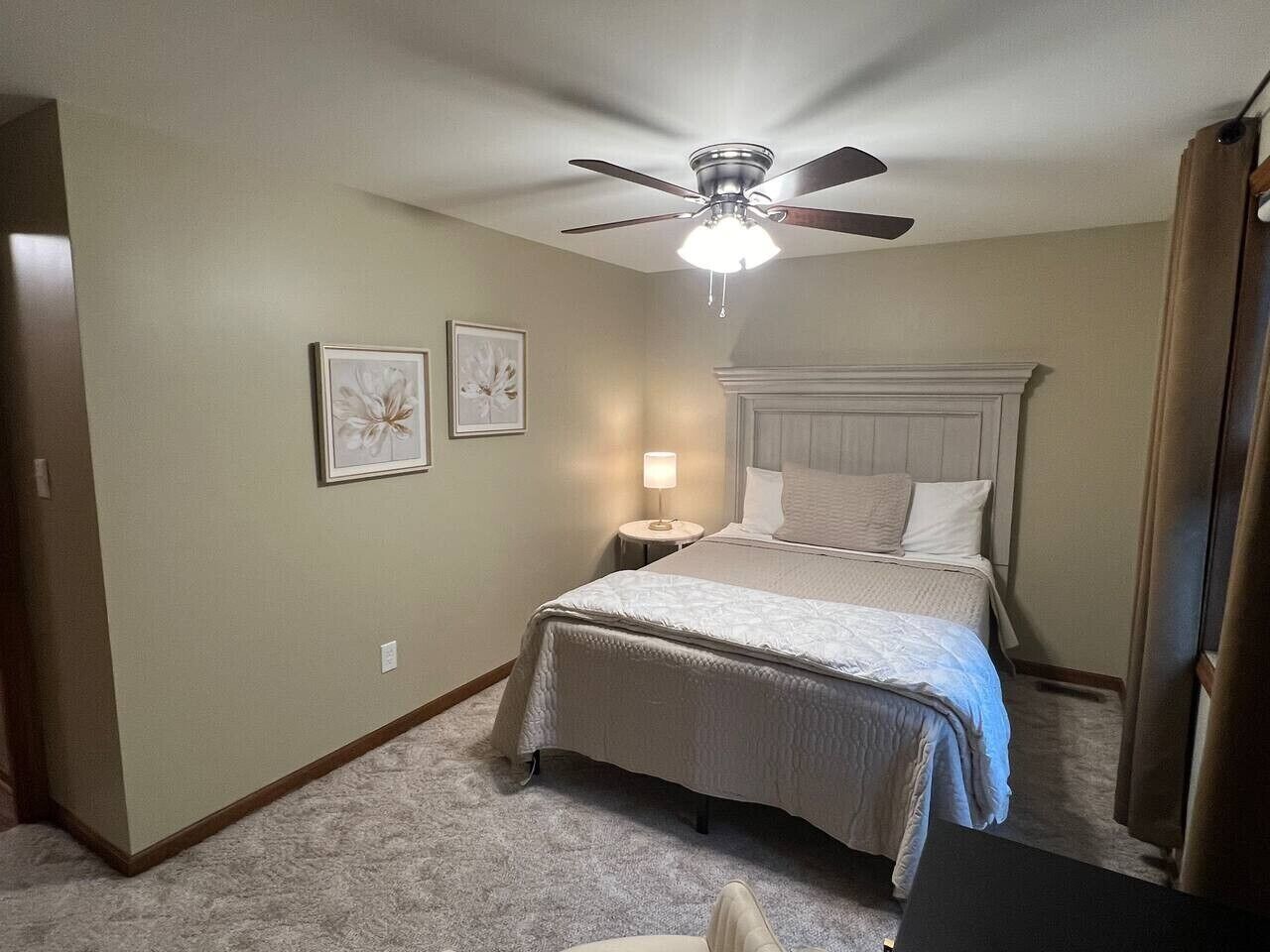 Un dormitorio con cama, ventilador de techo, mesita de noche y cuadros en la pared.