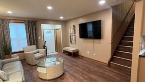 A living room with a sofa, armchair, coffee table, and a TV mounted on the wall.