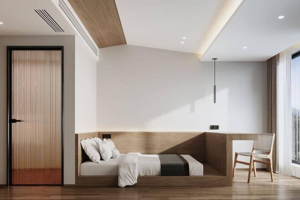 Ein modernes Hotelzimmer mit einem hölzernen Kopfteil, einer Schlafcouch, einem Sessel und einem großen Fenster.