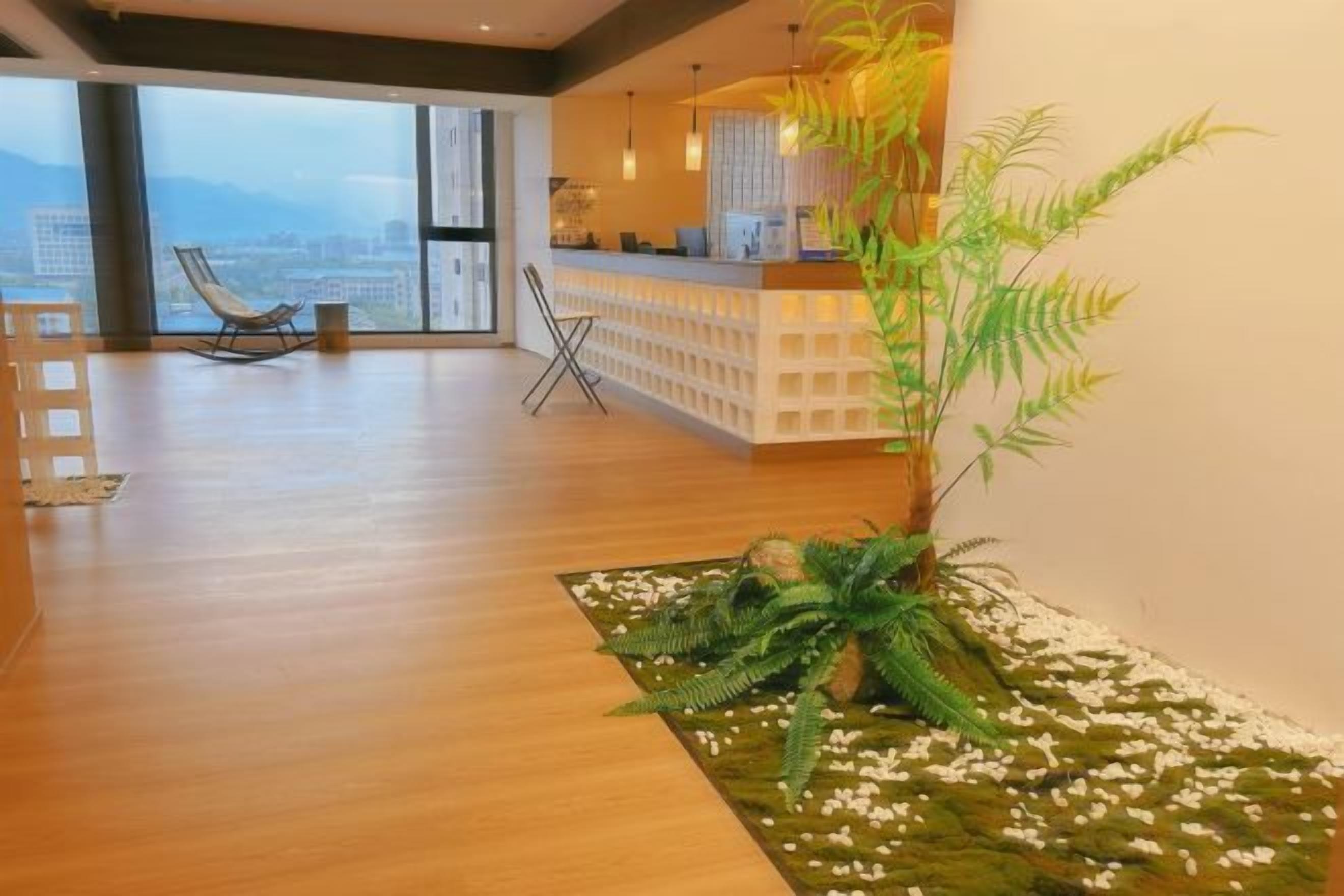 Um quarto amplo com piso de madeira, balcão de recepção, área de estar com cadeiras e uma grande janela com vista para a cidade.