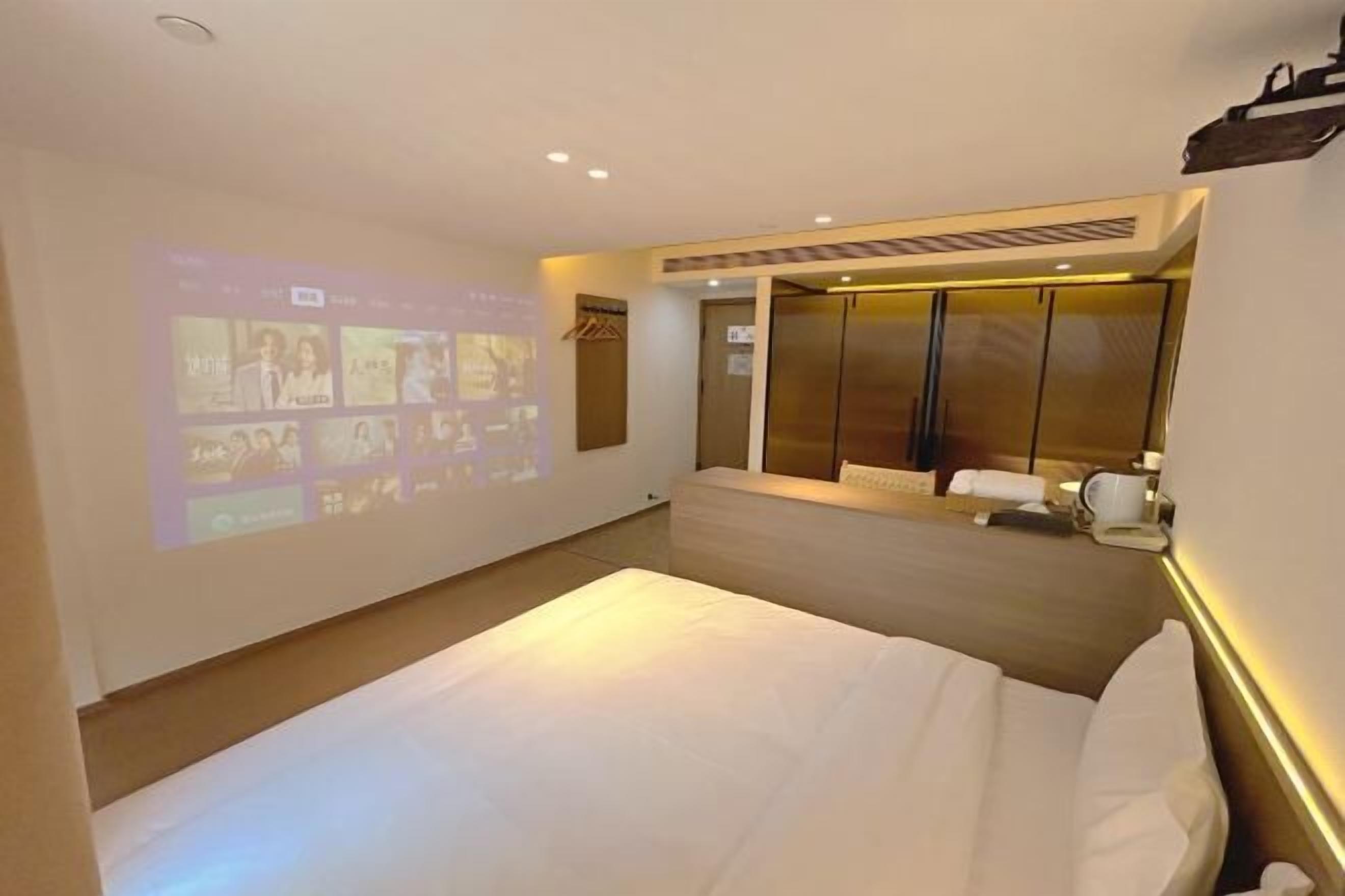 A hotel room with a bed, a wall-mounted TV, a wardrobe, and a seating area with a table and chairs.