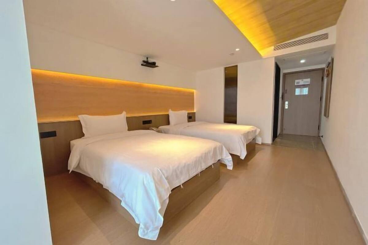Ein Hotelzimmer mit zwei Betten, einem Holzkopfende und einem modernen Deckenstil.