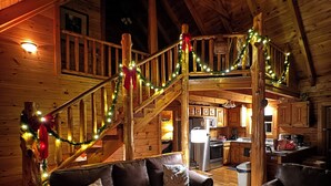 A cozy cabin interior with a wooden staircase decorated with lights, a leather sofa, and a wooden table. - Family Cabin with Hot Tub, Game Room & Pool Access (Pigeon Forge)