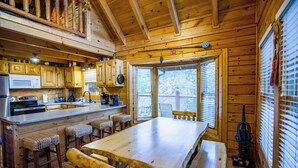 A wooden cabin interior with a kitchen, dining area, and a large window. - Family Cabin with Hot Tub, Game Room & Pool Access (Pigeon Forge)