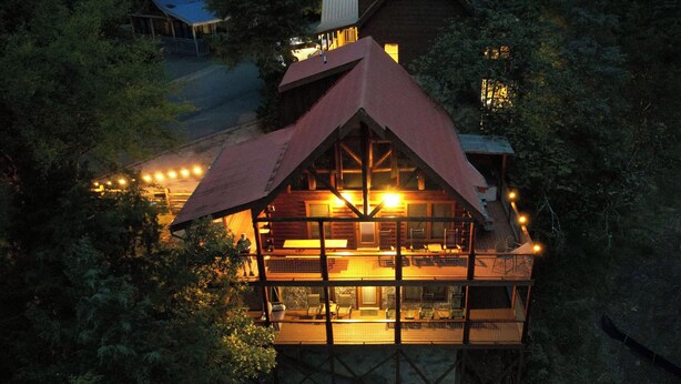 A two-story wooden cabin with a sloped roof, surrounded by trees. - Family Cabin with Hot Tub, Game Room & Pool Access (Pigeon Forge)
