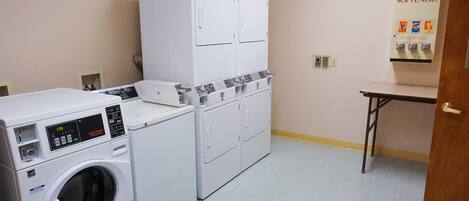 A laundry room with a front-loading washer and dryer, a cabinet with shelves, and a soap and bleach dispenser.