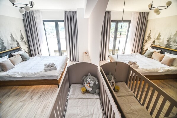 A hotel room with two beds, a crib, and large windows with curtains.