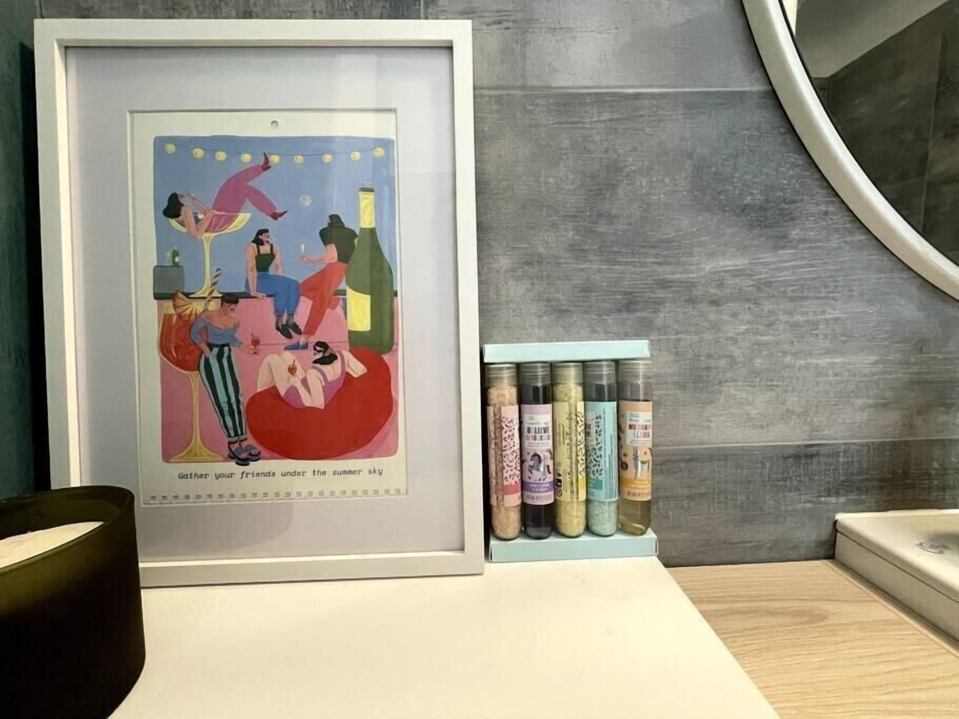 A framed artwork depicting a social scene with people and a bottle, placed on a counter next to a row of condiment bottles.