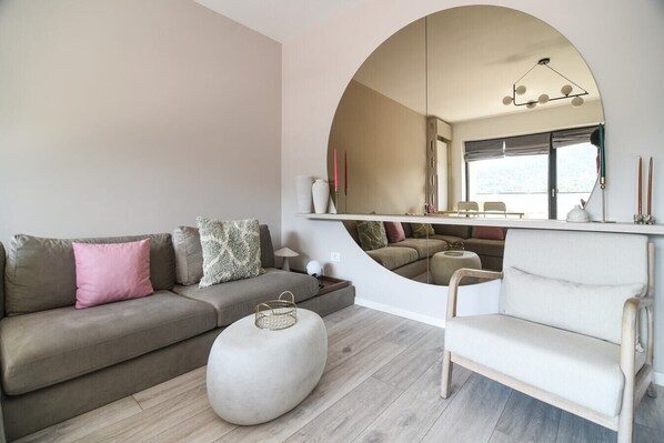 A modern living room with a large round mirror, a grey sofa, a white armchair, and a round ottoman.