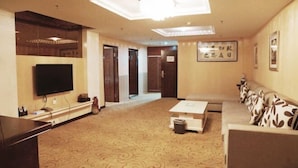 A hotel room with a flat-screen TV, a sofa, a coffee table, a patterned carpet, and a ceiling light fixture. - Xinranlin Hostel (Urumqi)
