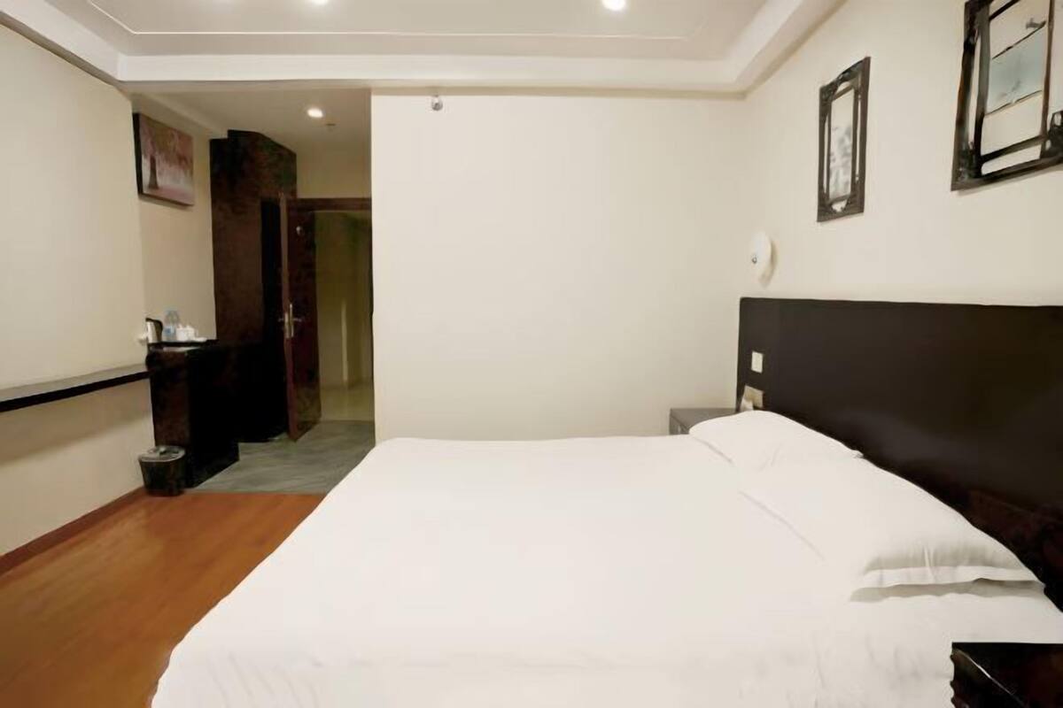 A bedroom with a large bed, a nightstand, a dresser, and a door leading to another room.