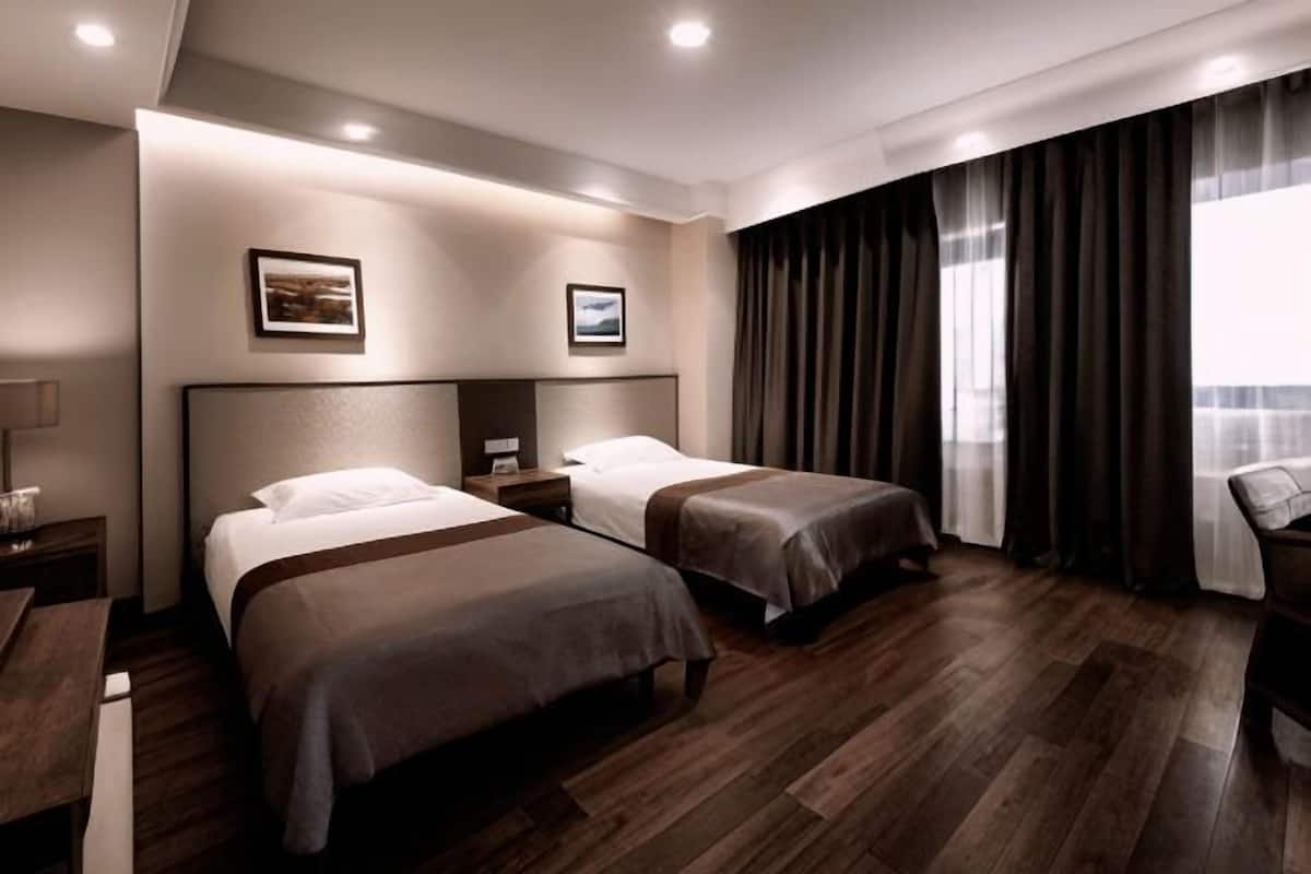 A hotel room with two beds, a desk, a chair, and a large window with curtains.