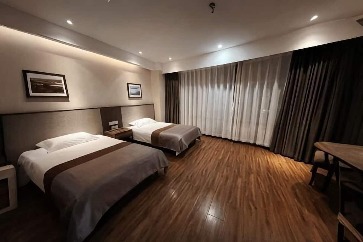 A hotel room with two beds, a desk, a chair, a window with curtains, and a picture on the wall.