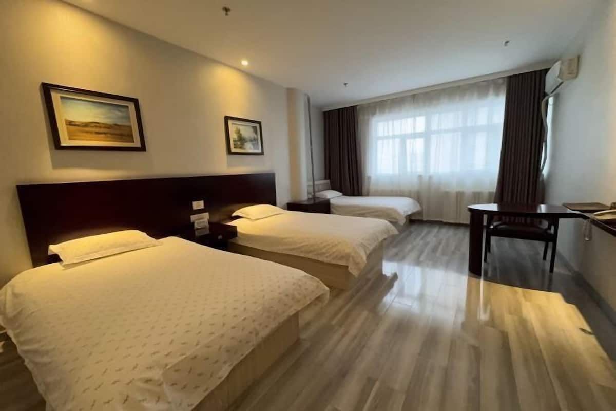 A hotel room with two beds, a desk, and a large window with curtains.