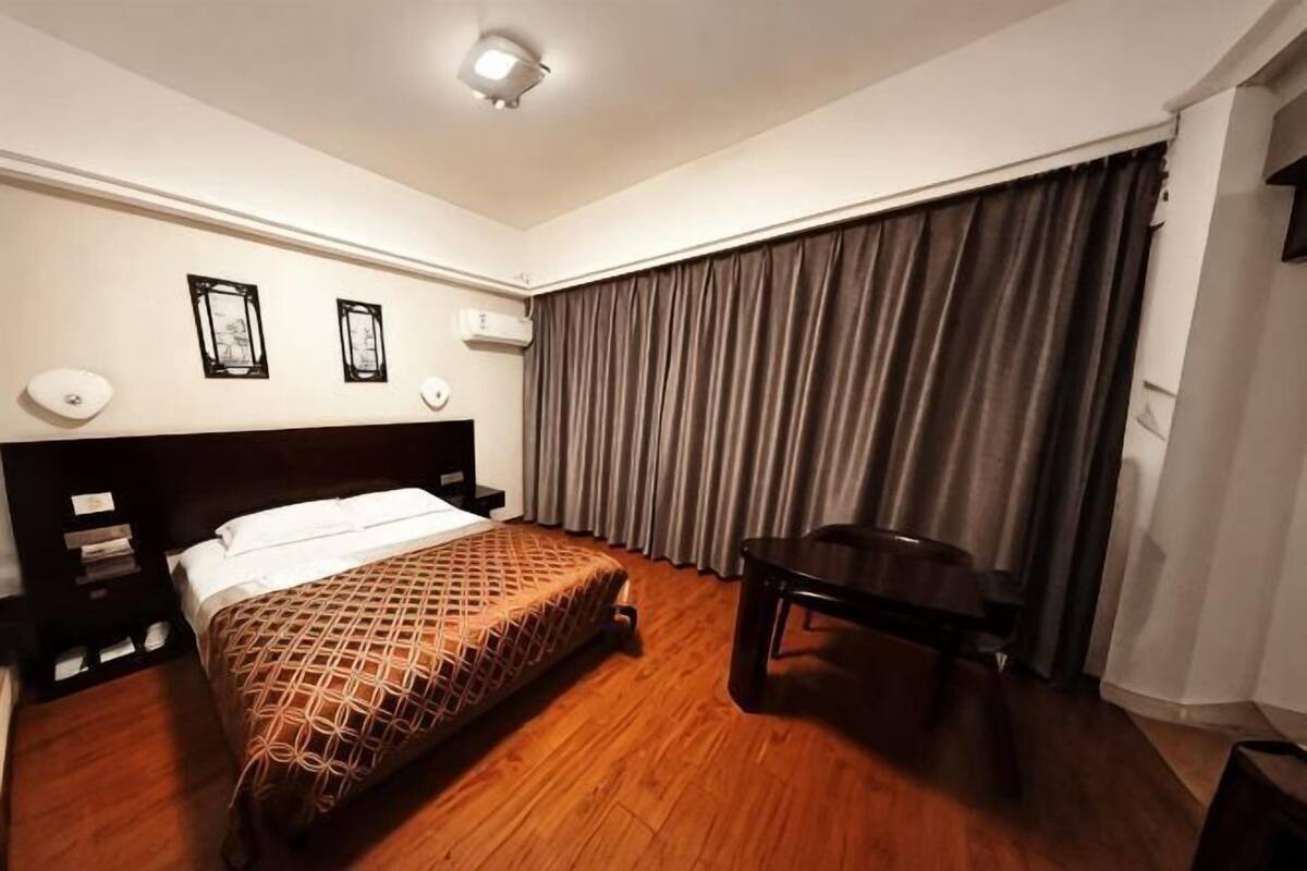 A hotel room with a wooden floor, a bed with a patterned bedspread, a desk, and a chair.