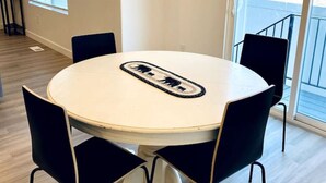 Uma sala de jantar com uma mesa redonda, cadeiras pretas, um lustre, uma frase inspiradora emoldurada e vista através de uma grande janela.