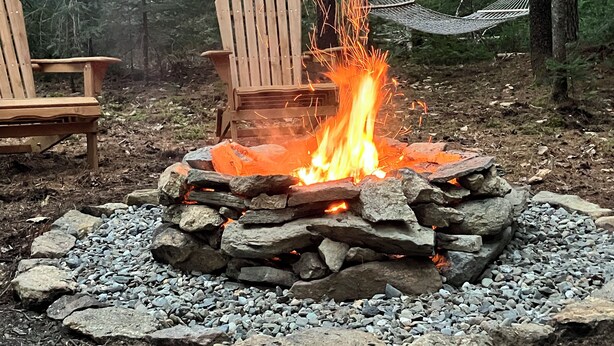 Una fogata rodeada de rocas y dos sillas de madera tipo Adirondack.