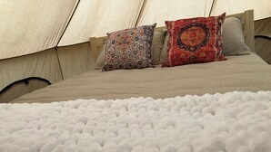 Una cama con una manta blanca con textura, dos almohadas estampadas y un cabecero color beige.