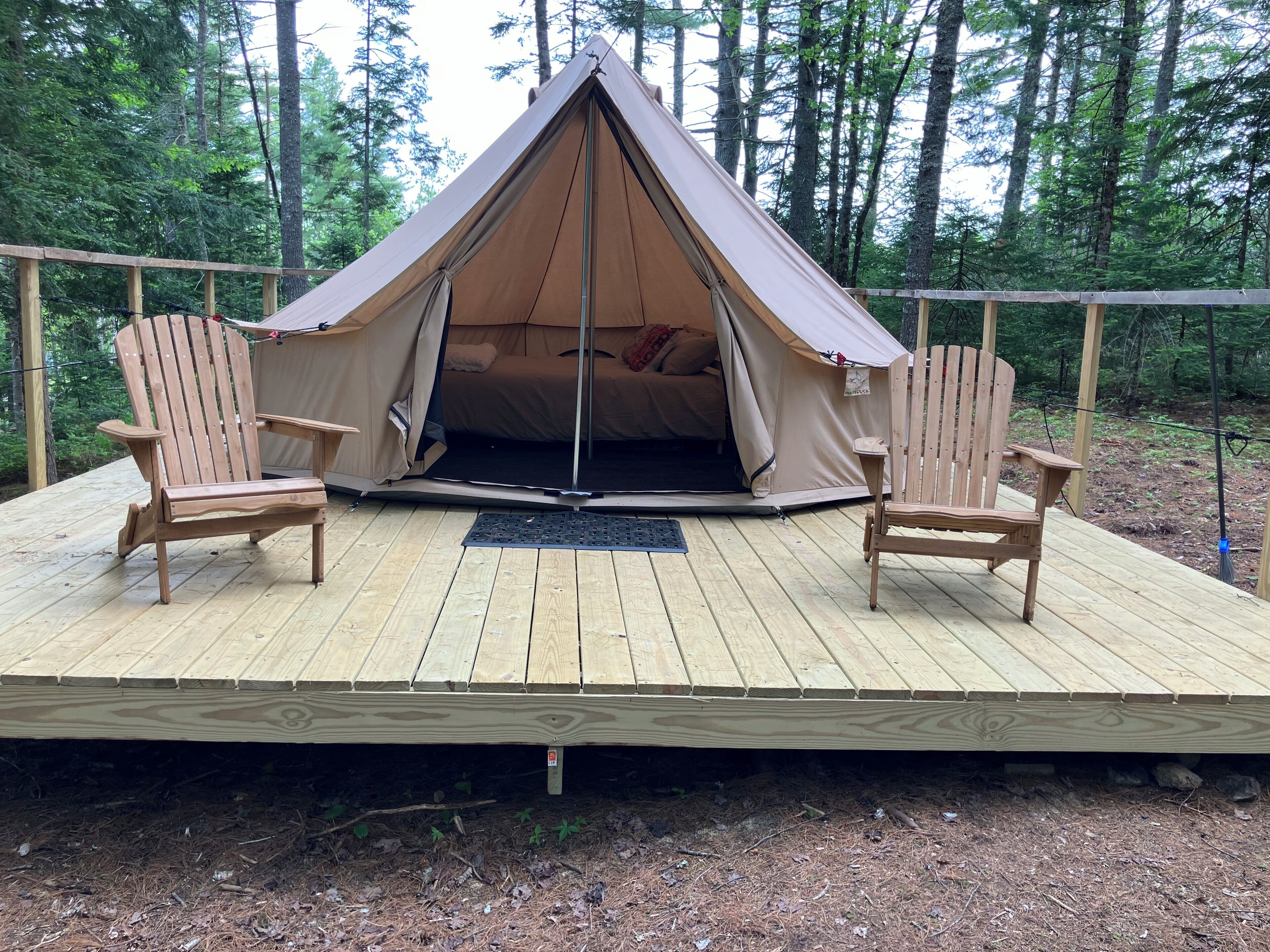 A tent with a bed inside, two wooden chairs, and a wooden deck.