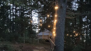 Una escalera de madera que lleva a una casa rodeada de árboles, con luces colgantes a lo largo del camino.