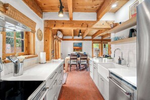 Une cuisine moderne avec des poutres en bois, des meubles blancs et un coin repas comprenant une table et des chaises.