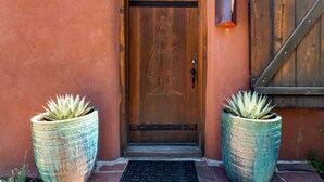 A wooden door with a metal handle, flanked by two large potted plants. - Luxury Home, Walk to Canyon Road, Historic Plaza (Santa Fe)