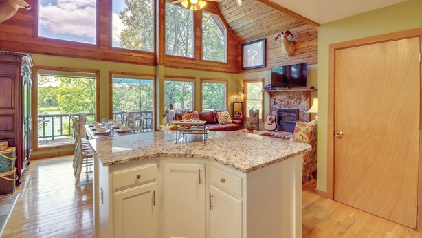 A spacious kitchen with a large island, wooden ceiling, and large windows offering views of the outdoors. - Peaceful Greers Ferry Cabin w/ Deck & Lake View! (Greers Ferry)