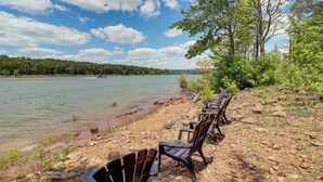 A lakeside view with chairs along the shore, a clear sky, and a forested landscape in the background. - Peaceful Greers Ferry Cabin w/ Deck & Lake View! (Greers Ferry)