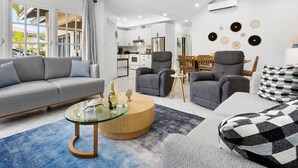 A modern living room with a grey sofa, two armchairs, a glass coffee table, and a patterned throw pillow. - Cozy 3BR Town Home in Gated Community @ Palm Beach (Noord)