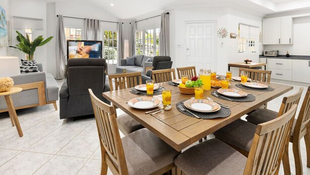 A modern dining room with a wooden table set for six, surrounded by cushioned chairs. - Cozy 3BR Town Home in Gated Community @ Palm Beach (Noord)